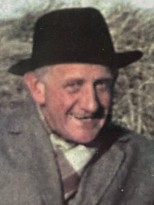 A photo of my grandfather, Felix Maurice Rose, in a homburg hat and overcoat, sitting on the beach, grinning cheekily. He was a conscientious objector