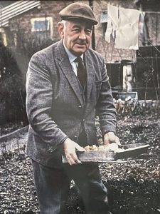 A photo of my grandfather, Harold James Aburrow, wearing a flat cap and a suit, standing in the garden, holding a tray of onions